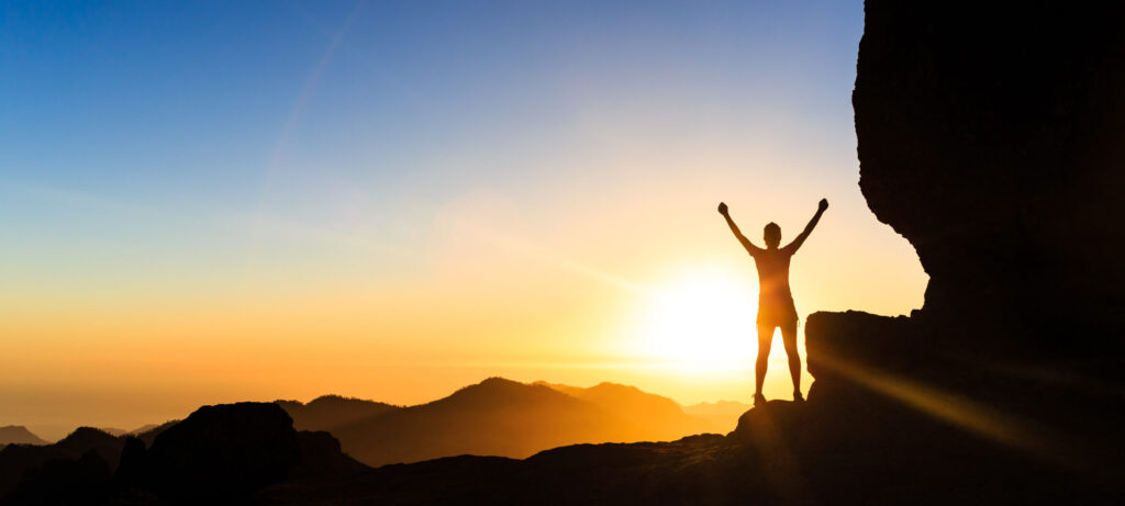 A happy person standing on top of a mountain looking at the sunrise