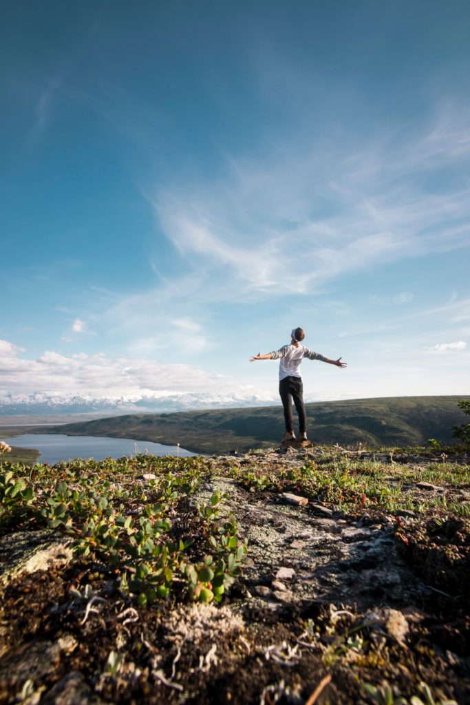 Person standing above a lake with arms outstretched