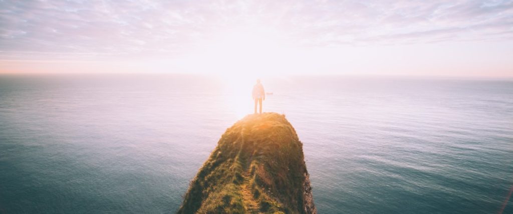 Person standing on top of a cliff at sunrise