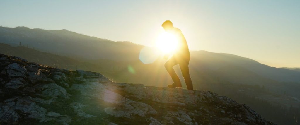 A person climbing a mountain as the sun rises